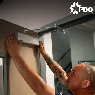 A maintenance man maintaining a door closer within a commercial building.