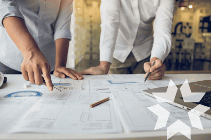 Two engineers looking at blueprints laid out on a table. The PDQ Star appears in the bottom right corner of the image