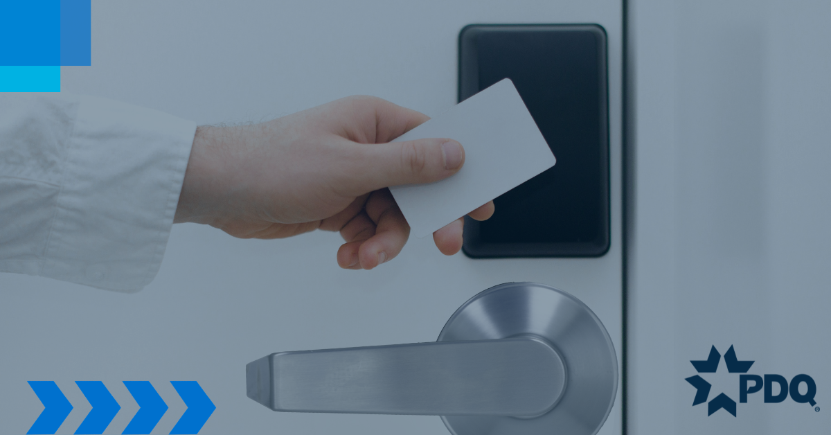 A person in a white shirt holding a key card up to a black card reader mounted on a wall above a satin chrome lever door handle.