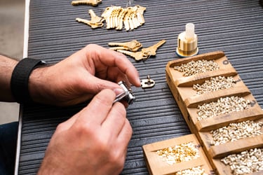 Locksmith hand-pinning a lock core, placing pins from a sorted pin kit tray, with cut keys and oil bottle nearby.