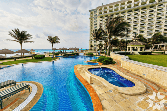 Exterior of a pool with a hotel in the background near a beach. The PDQ Star appears in the bottom right corner of the image.