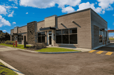 Modern commercial building exterior with wood siding, stone accent, glass storefront, and drive-thru lane