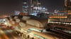 Nighttime view of KAFD Metro Station in Riyadh, showing its illuminated lattice-shell roof structure with a train on the elevated platform and the King Abdullah Financial District skyline in the background.