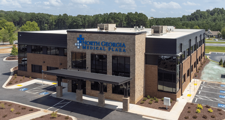 Aerial view of North Georgia Medical Plaza, a two-story stone and brick medical office building with a covered entrance canopy, large windows, and a landscaped parking lot surrounded by trees.