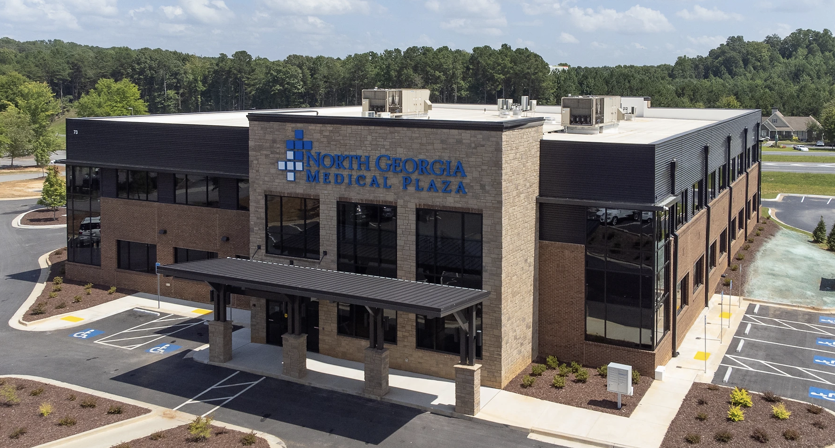 Aerial view of North Georgia Medical Plaza, a two-story stone and brick medical office building with a covered entrance canopy, large windows, and a landscaped parking lot surrounded by trees.